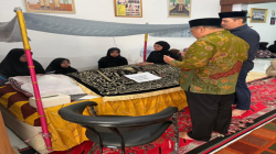 Suasana takziah di rumah duka, beberapa perempuan berjilbab duduk di samping jenazah yang tertutup kain bermotif